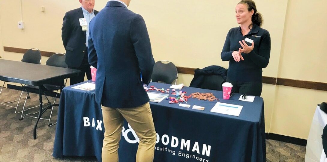 ITE Illinois Student Day 2019 - A man in a blue blazer and khakis is standing and speaking to a woman in a black shirt who is standing behind the table.