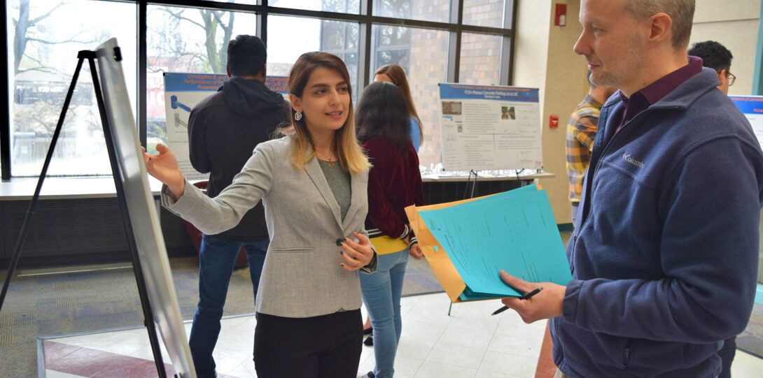 ITE members participating in the CME Poster competition - A poster session with a woman in a gray blazer pointing at a research poster on an easel and explaining it to a man in a blue sweatshirt.